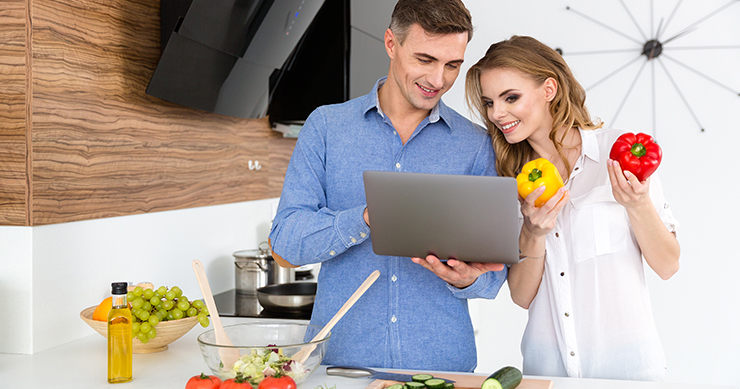 Man and Woman preparing food and looking at the laptop
