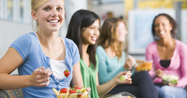 Happy Girl eating fruits withs friends in the background