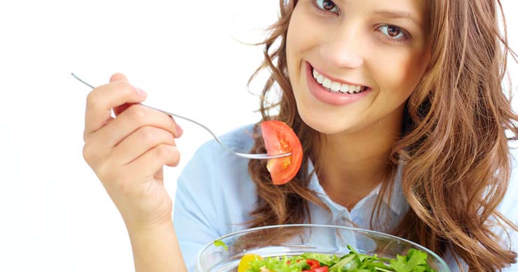 Smiling girl eating a salad with white background